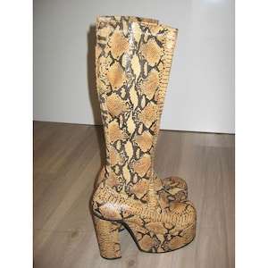 Puede incluir: Botas altas de plataforma con estampado de piel de serpiente en tonos beige, marrón y negro. Las botas tienen un tacón grueso y una puntera redondeada. La caña de la bota llega hasta la rodilla.