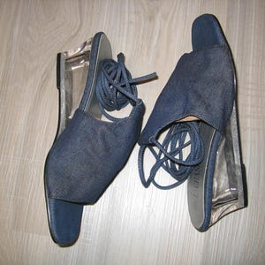 Könnte beinhalten: Ein Paar blaue Jeans-Keil-Sandalen mit durchsichtigen Kunststoffabsätzen und Schnürsenkeln. Die Sandalen haben ein Kreuzschnürdesign und sind am Knöchel gebunden.