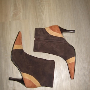 May include: A pair of brown suede ankle boots with pointed toes and high heels. The boots feature tan and light brown accents on the toe and ankle. The heels are dark brown.