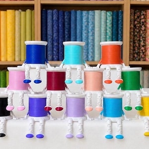 May include: A pyramid arrangement of twelve colorful sewing thread spools, each featuring white articulated plastic legs and feet. The spools are in shades of blue, turquoise, orange, pink, maroon, peach, green, black, purple, lavender, and yellow.