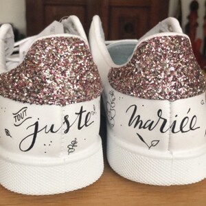 May include: A pair of white trainers with pink glitter on the back. The left shoe says "Tout juste" and the right shoe says "mari&eacute;e".