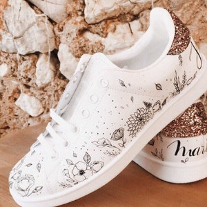 May include: White canvas sneakers with black floral designs and gold glitter accents. The right shoe has the word "married" written on the side.