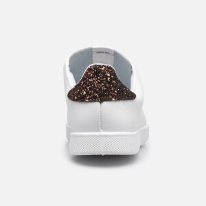 May include: White leather trainers with a brown glitter accent on the back of the shoe.