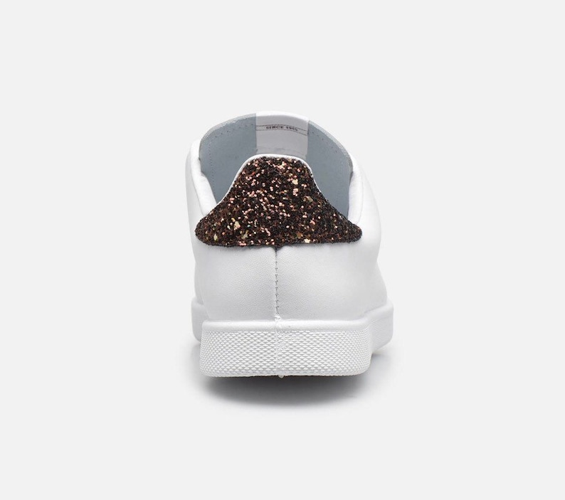 May include: White leather trainers with a brown glitter accent on the back of the shoe.