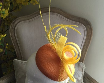 Lovely orange round fascinator with yellow loops, feathers and netting. Stunning!
