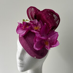 Magentafarbener Steifheits-Fascinator mit magentafarbenen Schleifen aus Abaca-Seide, lilanen Blumen und Orchideenblüten.