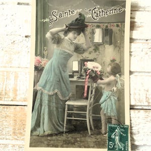 Postal antigua de Cupido: niña pequeña, alas de ángel querubín, lazo, modista francesa, sombrero de vestir, tintada, 1900