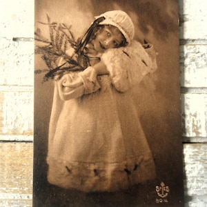 Postal navideña antigua: niña pequeña, gorro de invierno eduardiano, manguito de piel, rama de pino, sepia francesa de 1900