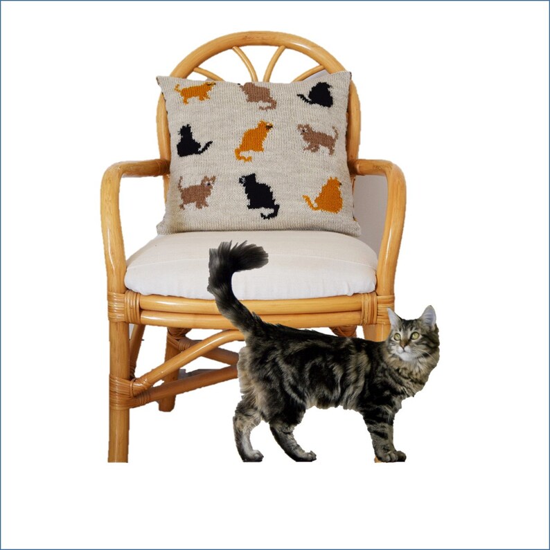 May include: A woven pillow with cat silhouettes in various colors rests on a wicker chair with a white cushion. A tabby cat with a fluffy tail stands nearby. The pillow features brown, black, and orange cat designs.
