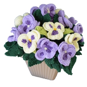 May include: A crocheted potted plant with purple and cream flowers. The plant is in a brown pot with a ribbed texture.