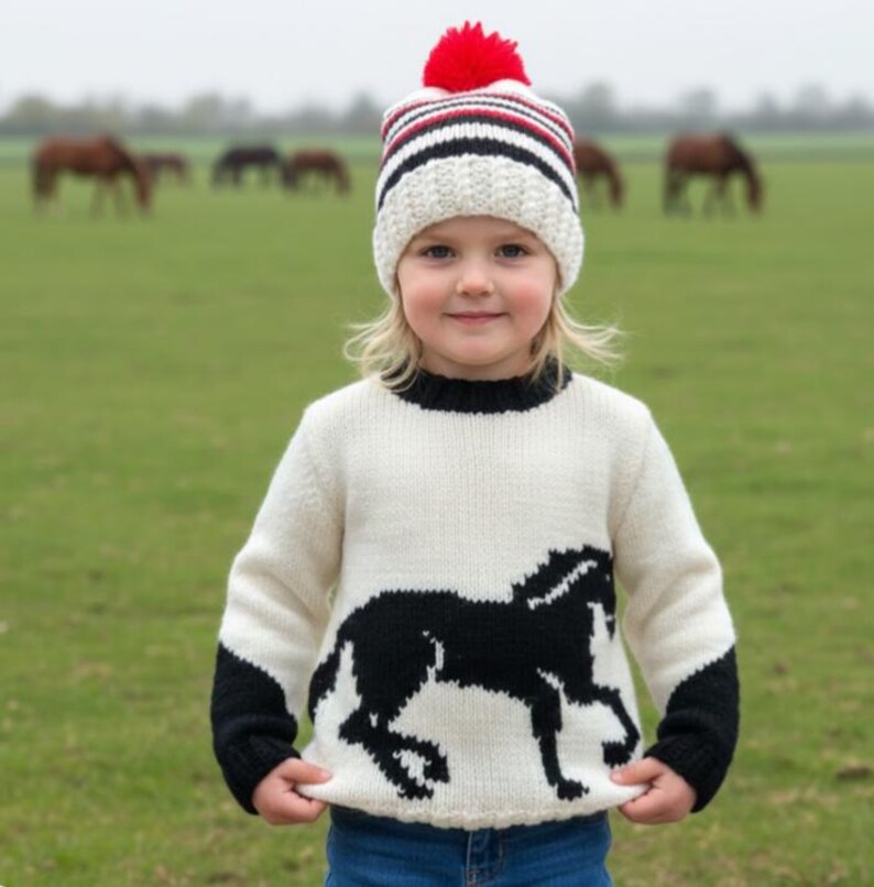 May include: A cream-colored knit sweater featuring a large black horse silhouette on the front, black cuffs, and a black neckline. The outfit includes a matching cream, black, and red striped knit beanie with a red pom-pom on top.