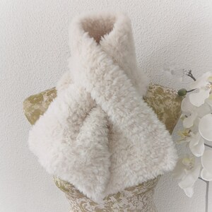 May include: A white faux fur scarf with a soft, fluffy texture. The scarf is folded and displayed on a mannequin.