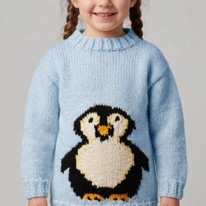 May include: A light blue knitted sweater featuring a large penguin design on the front. The penguin has a white belly, black body, and yellow beak. The sweater has a ribbed neckline, cuffs, and hem.