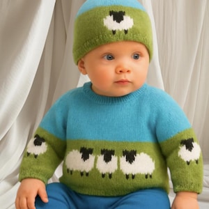 Peut inclure: Un bébé portant un ensemble tricoté bleu et vert. Le pull présente une bande verte avec des moutons blancs, et le chapeau a un seul mouton. Le bébé porte également un pantalon bleu.