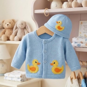 May include: A light blue baby cardigan and matching hat set. The knitted cardigan features two yellow and orange duck appliques. The hat also has a duck applique. The set is displayed on a wooden hanger.