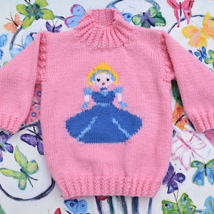 May include: Pink knitted jumper with a cartoon princess design in blue and yellow.