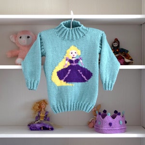 May include: A light blue knitted sweater with a long-sleeved design features a colorful embroidered image of a princess with long blonde hair.
