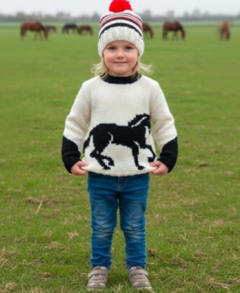 May include: A white knitted sweater featuring a black horse silhouette on the front and black cuffs, paired with blue denim jeans and a white, black, and red striped knit beanie with a red pom-pom on top.