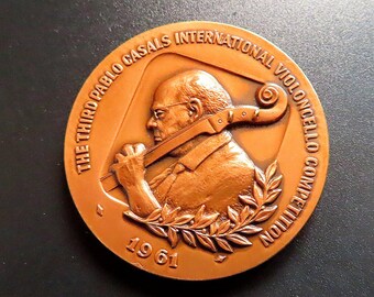 Puede incluir: Una medalla de bronce que conmemora el tercer Concurso Internacional de Violonchelo Pablo Casals, celebrado en 1961. La medalla presenta un perfil de Pablo Casals sosteniendo un violonchelo.