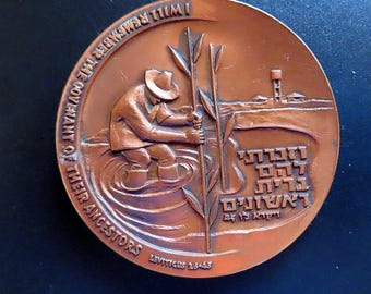 Puede incluir: Una medalla conmemorativa circular de tono cobre con un relieve de una figura con sombrero de pie en el agua sosteniendo juncos altos. El texto dice I WILL REMEMBER THE COVENANT OF THEIR ANCESTORS, LEVITICUS 26:45, y caracteres hebreos.