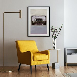 May include: A framed wall art print featuring a detailed illustration of a black BASF chrome cassette tape with the text BASF chrome 120, displayed in a room with a yellow armchair, a gold floor lamp, and a glass vase with purple flowers.