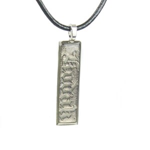 May include: A silver pendant necklace with a black leather cord. The pendant is rectangular and features the word "Forever" in a gothic font.