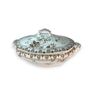 May include: Oval, lidded serving dish with a floral pattern in brown and white. The dish has a handle on the lid and two side handles. The rim of the dish and lid are decorated with a repeating leaf design. A classic piece for serving.