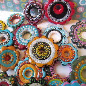 May include: A collection of colorful, hand-painted ceramic round ornaments with a hole in the center. Each ornament features a different pattern and design, including polka dots, stripes, and swirls.