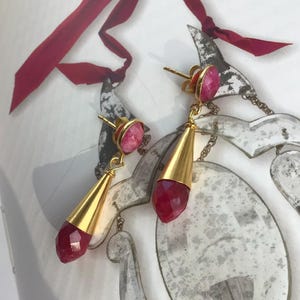 Puede incluir: Un par de pendientes de oro con gotas de piedras preciosas rosas. Los pendientes tienen una pieza de oro en forma de cono con una piedra preciosa rosa en la parte inferior.