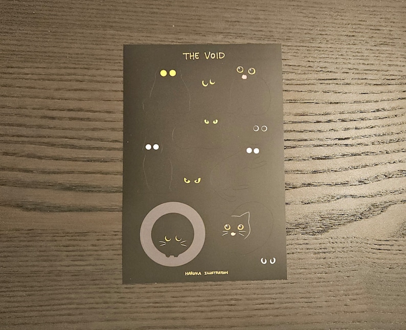 Op de afbeelding: Zwarte kaart met de tekst "THE VOID" en illustraties van kattenogen en gezichten. De ogen zijn geel en wit. De tekst "HARUKA ILLUSTRATION" is ook aanwezig.