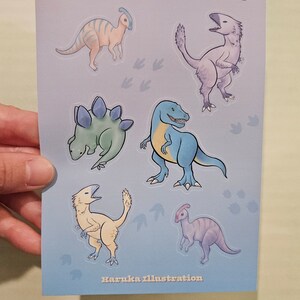 Op de afbeelding: Een lichtblauwe kaart met cartoon-dinosaurussen in verschillende kleuren. Het woord "PASTELOSAURUS" staat bovenaan gedrukt. De naam van de kunstenaar, "Haruka illustration", staat onderaan gedrukt.