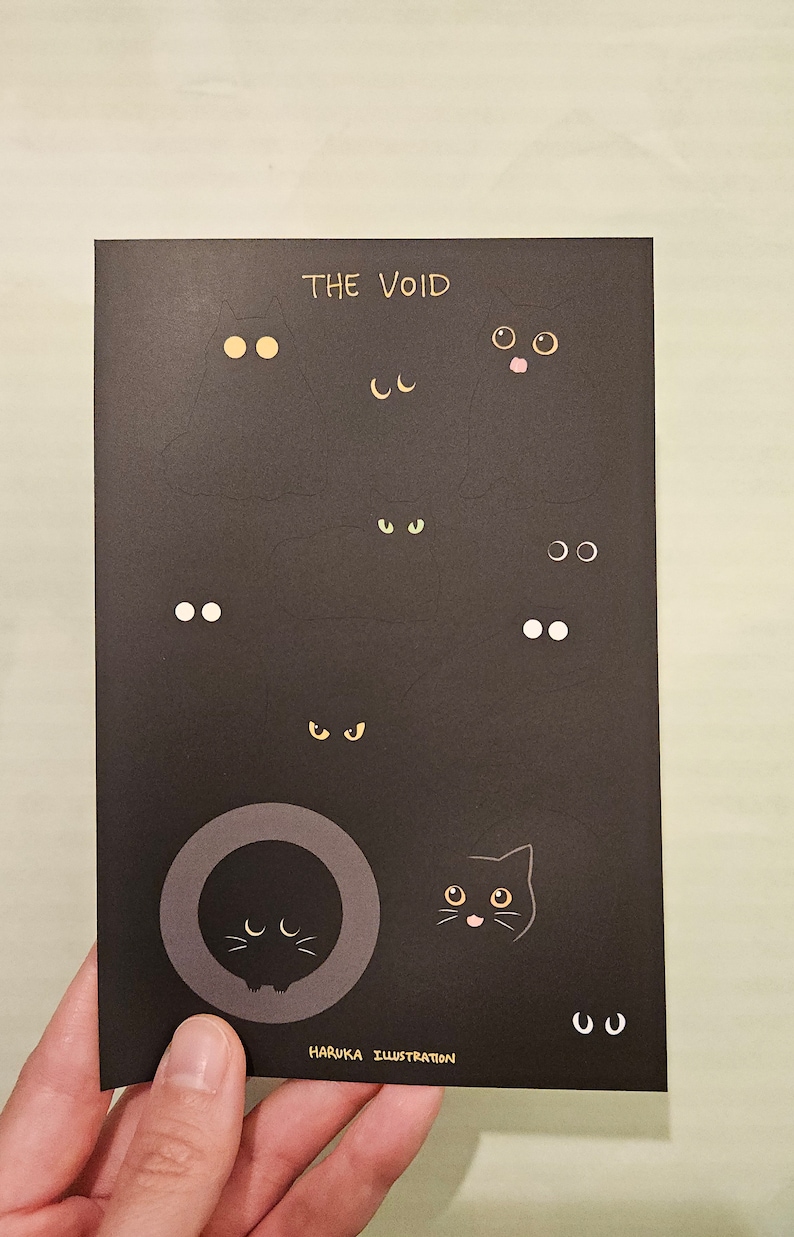 Op de afbeelding: Zwarte kaart met de tekst "THE VOID" en diverse illustraties van kattenogen. De ogen zijn in verschillende kleuren en vormen. De kaart bevat ook de tekst "HARUKA ILLUSTRATION".