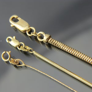 May include: Three gold chains with different styles of links. The chains are on a grey surface.