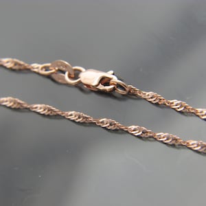 May include: A rose gold necklace with a delicate twisted rope chain design. The chain is secured with a lobster clasp. The necklace is displayed against a dark background.