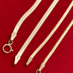 Puede incluir: Tres cadenas de serpiente de oro con cierres. Las cadenas están sobre un fondo rojo.