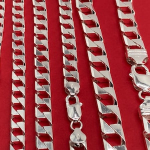 Peut inclure: Une collection de six chaînes à maillons gourmette de couleur argentée disposées verticalement. Chaque chaîne présente des maillons plats polis et imbriqués ainsi qu'un fermoir mousqueton sécurisé, avec une finition métallique uniforme.