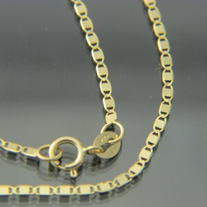 May include: A close-up of a gold necklace with a delicate chain design. The chain features small, rectangular links connected in a repeating pattern. The necklace has a spring ring clasp for secure closure.