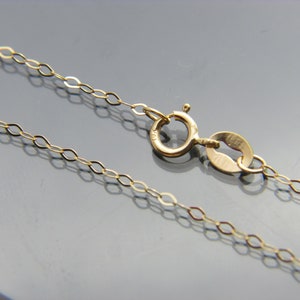 May include: A gold chain necklace with a lobster clasp fastening. The chain is made of small, oval-shaped links.