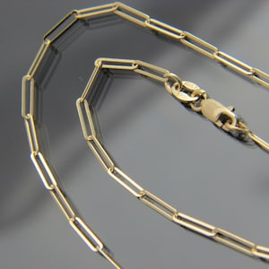 May include: A gold chain necklace with a lobster clasp closure. The chain is made of small, rectangular links.