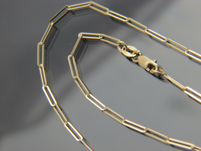 May include: A gold chain necklace with a lobster clasp closure. The chain is made of small, rectangular links.
