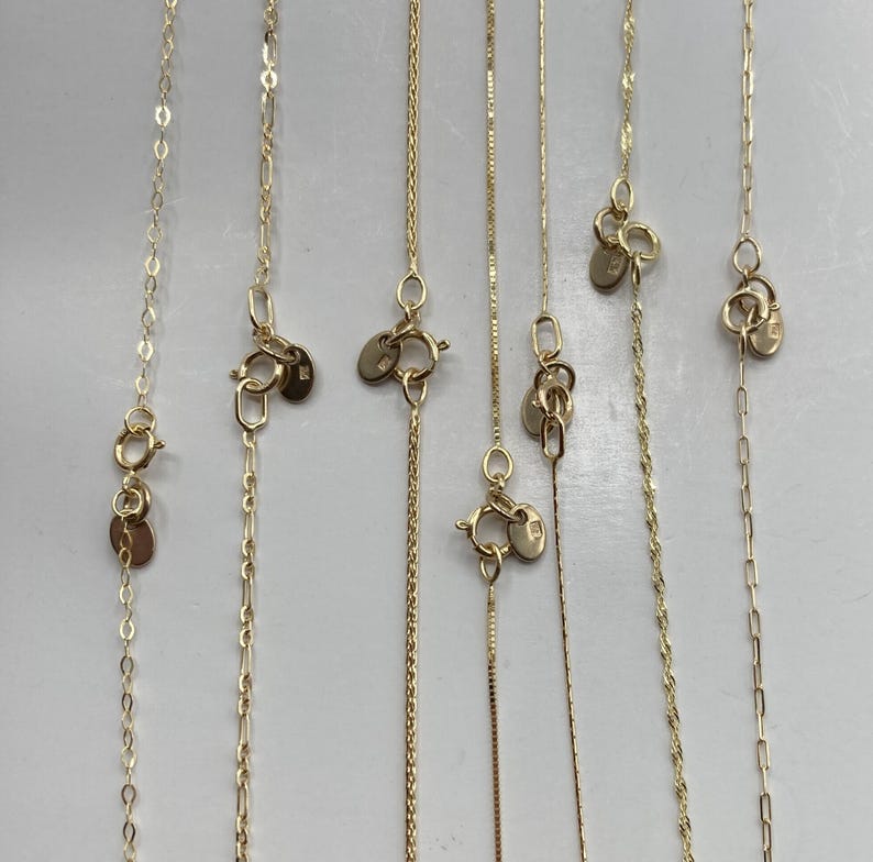 May include: A selection of gold necklaces, each with a different chain design. The image shows close-ups of the clasps and tags. Chain styles include box, cable, and rope, all in a warm gold colour.