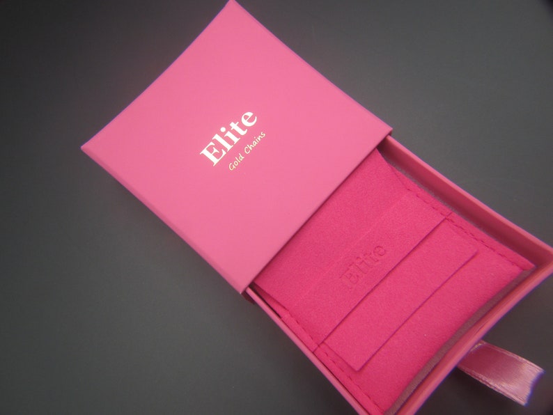 May include: A vibrant pink jewellery box, branded with "Elite Gold Chains" in white. Inside, a pink pouch is visible, also bearing the brand name. A pink ribbon adds a finishing touch.