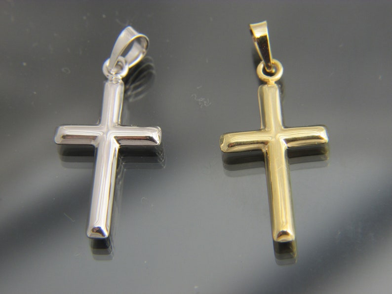 May include: Two simple cross pendants, one silver and one gold, on a reflective surface.