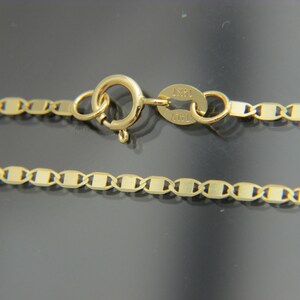 May include: A gold necklace with a flat-link chain design. The necklace has a lobster clasp and a tag marked "14KT ITALY". The chain is made of small, rectangular links. The necklace is likely made of 14-carat gold.