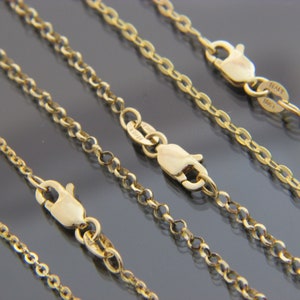 May include: Five gold chains of varying lengths, all with lobster claw clasps. The chains are arranged in a staggered pattern on a grey surface.