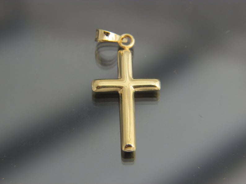May include: A gold-colored cross pendant with a simple design. The pendant has a loop at the top for attaching to a chain.