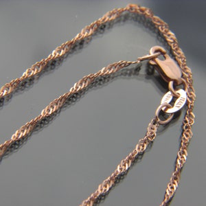 May include: Close-up of a rose gold necklace with a twisted rope chain design. The clasp is visible, with a small tag that reads "10K ITALY". The chain is a warm, metallic color.