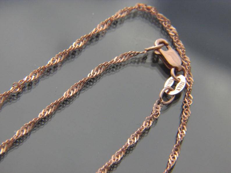 May include: Close-up of a rose gold necklace with a twisted rope chain design. The clasp is visible, with a small tag that reads "10K ITALY". The chain is a warm, metallic color.