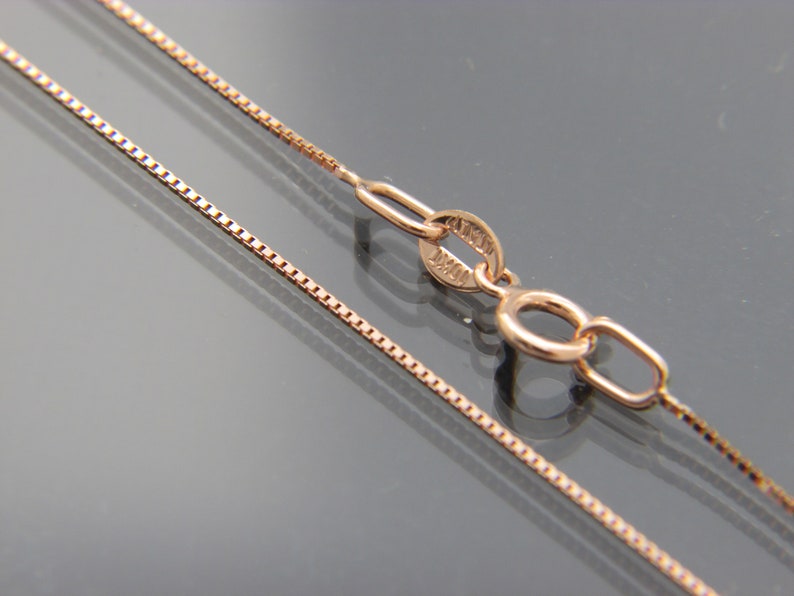 May include: A rose gold chain necklace with a box clasp. The chain is made of small, square links.