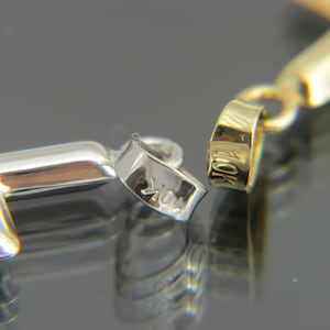 May include: A close-up of a silver cross pendant with a 10K hallmark. The pendant is attached to a gold chain.